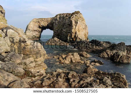 The warm winter sun shining down on the coastline of County Donegal, Ireland on a fresh, hazy day in winter with a magnificent rocky outcrop forming a natural arch in the Atlantic Ocean. 
