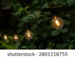 Warm yellow string lights and small bulbs hang outside the coffee shop, casting warm glows in the misty mountain forest, creating a poetic night scene with red flowers and green plants.