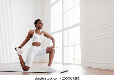 Warming Up Before Workout. Smiling Sporty Black Woman Training At Home Or Fitness Club Studio, Beautiful Female Stretching Legs After Exercises On Mat, Wearing White Bra And Bike Shorts, Free Space