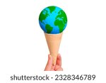 Warming and climate change concept: Hand holding a miniature globe nestled within a delicious ice cream waffle cone isolated on white background with copy space.