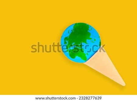 Warming and climate change concept: Miniature globe nestled within a delicious ice cream waffle cone isolated on yellow background with copy space.