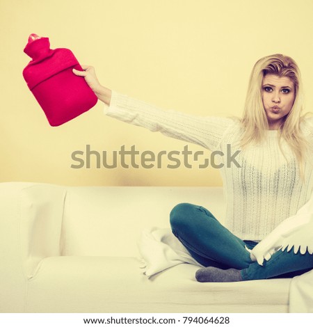 Warming up during cold winter or autumn days. Woman sitting on couch holding hot water bottle