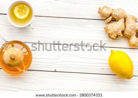 Warming tea with lemon and ginger. Cup, teapot, ginger root on white wooden background top view.