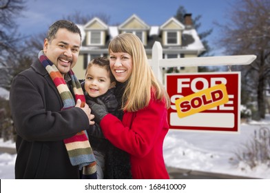 Warmly Dressed Young Mixed Race Family In Front Of Sold Home For Sale Real Estate Sign And House With Snow On The Ground.