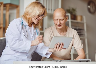 Warm-toned Portrait Of Bald Woman Looking At Digital Tablet During Consultation With Female Doctor On Alopecia And Cancer Recovery