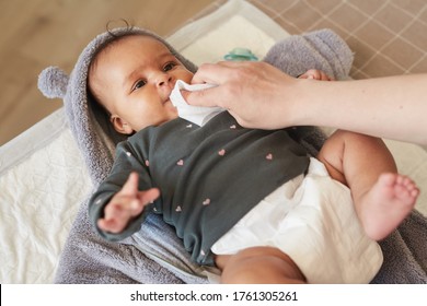 Warm-toned portrait of cute mixed-race baby on changing table with unrecognizable mother using wipes, copy space