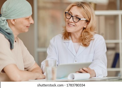 Warm-toned Portrait Of Smiling Female Doctor Talking To Bald Woman And Showing Data At Digital Tablet During Consultation On Alopecia And Cancer Recovery, Copy Space