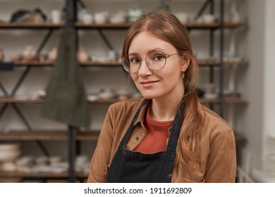 Warm-toned portrait of young female artisan looking at camera while posing in pottery workshop, hobby and small business concept, copy space - Shutterstock ID 1911692809