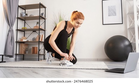 Warmup training. Online workout. Ready to exercise. Sport set. Smiling woman in activewear tie shoes looking on laptop at home interior. - Powered by Shutterstock