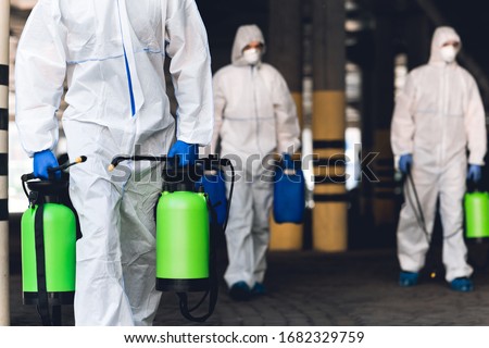 Warning, coronavirus disinfection. Men in virus protective suits carrying spray bottles with chemicals, blurred background