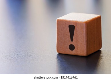 Warning exclamation mark on a wooden block to attract attention over a grey background with beams of light and copy space