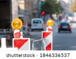 warning poles with orange light signal on the road about repairs work, blurred street with cars on background