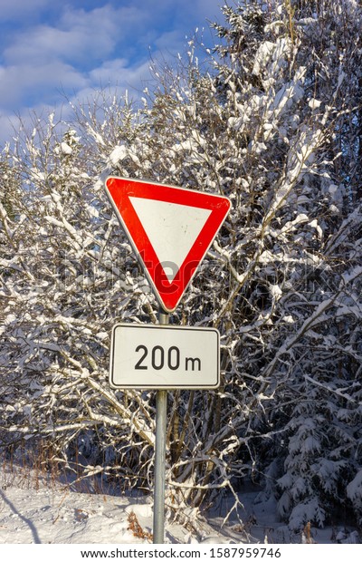 Warning\
road sign - give way. A sunny winter day.\
Latvia.