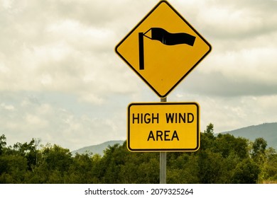 Warning Road Sign Of High Wind Area With Tree And Cloudy Sky Background