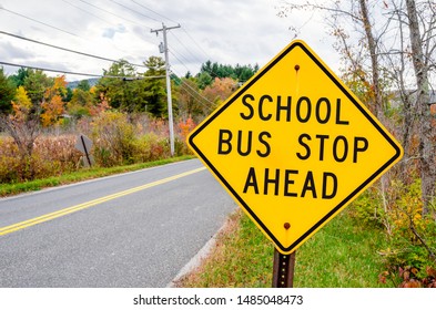 Warning Road Sign Telling Drivers That There Is A School Bus Stop Ahead. Cloudy Sky And Autumn Colours In Background. Back To School Concept.