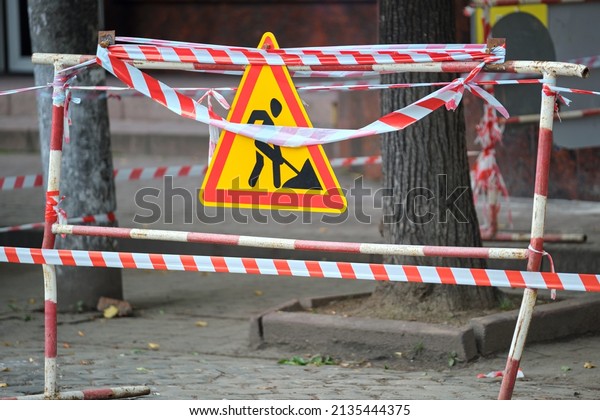 Warning roadworks sign and safety barrier on\
city street during maintenance repair\
work