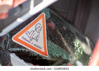 Warning Sign Of Children Inside A Car After An Accident With Bloody Broken Glass. Translation: Child In The Car. Close-up Of White Baby On Board Sticker On Car Back Window