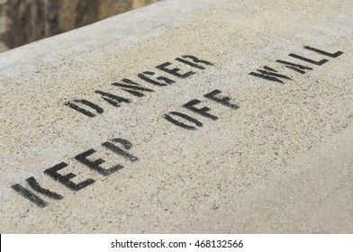 Warning sign 'DANGER KEEP OFF WALL' painted on a high concrete wall.