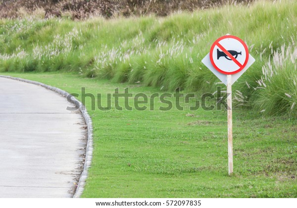 The warning sign do not use vehicle horn\
with flowering grass background of green golf course objective for\
do not disturbing golf\
players.