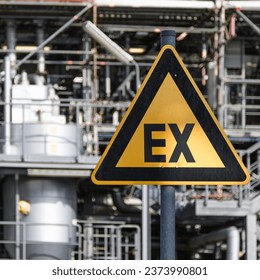Warning sign "explosive atmosphere" - the word "EX" on a yellow triangle with black borders - in front of a blurred industrial background