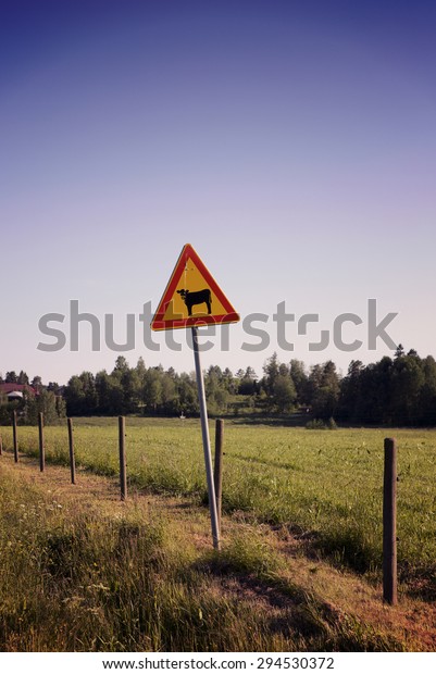 A warning sign on\
side of the road. This warning sign is for cattle. Image has a\
vintage effect applied. 