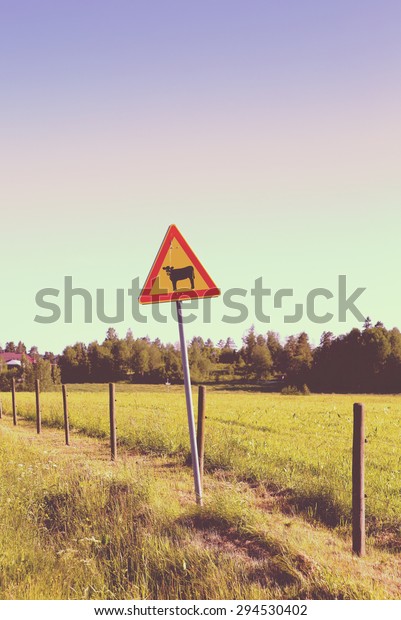 A warning sign on\
side of the road. This warning sign is for cattle. Image has a\
vintage effect applied. 