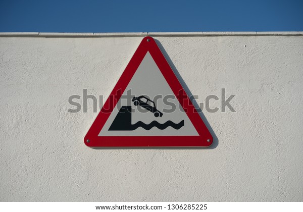 Warning sign, unprotected quayside or\
riverbank. Symbol of a car falling off the\
dock