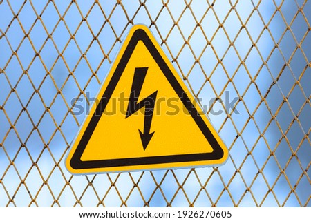 warning sign, yellow triangle with lightning on a fence made of metal mesh. 