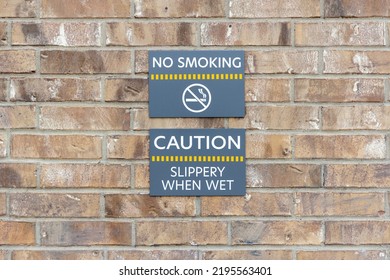 Warning Signs No Smoking And Slippery When Wet On Brick Wall, Warning Labels On Gray Plates.