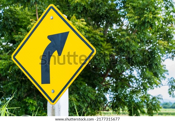 Warning traffic sign yellow turn right board on\
the road with cloud and blue\
sky.