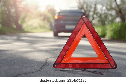 The warning triangle is at the back of the car at a safe distance.Car on the road behind warning triangle.The triangle placed behind the car. - Shutterstock ID 2314631185