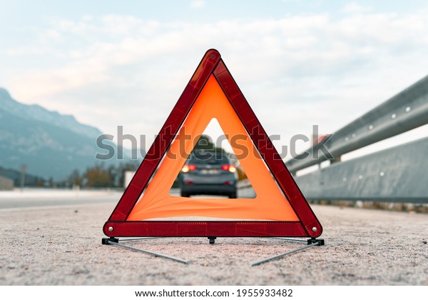 The warning triangle is at the back of the car at a\
safe distance.Car on the road behind warning triangle.The triangle\
placed behind the car.