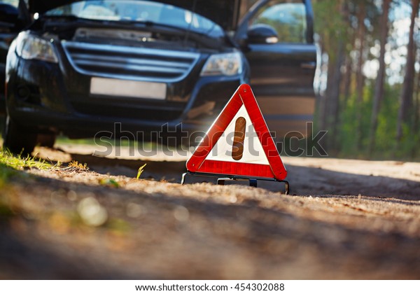 Warning triangle behind a broken down car.\
Selective Focus on red triangle warning\
sign.