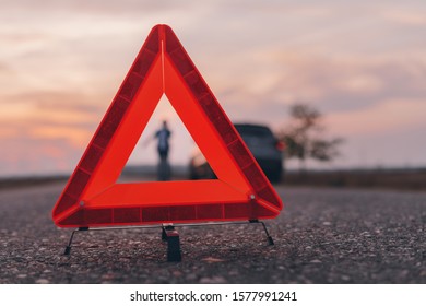 Warning triangle sign on the road, woman in blur background calling for roadside assistance by the broken car, selective focus - Shutterstock ID 1577991241