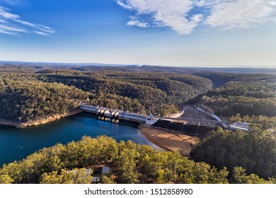 Warragamba dam of Sydney Water supply infrastructure on Nepean river forming fresh water lake between gum-tree woods. Aerial view over dam wall, bridge, gate and surrounding area.