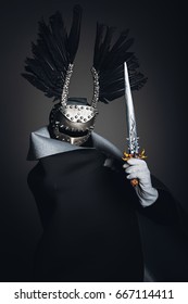 A warrior in a raincoat, a mask on his face and a silver knife in his hand, an image of a warrior on a black background
