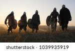 Warriors vikings stand in field and look at beautiful sunset on the battle field. Medieval Reenactment.Contre-jour. Back view.