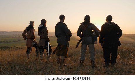 Warriors vikings stand in field and look at beautiful sunset on the battle field. Medieval Reenactment.Contre-jour. Back view.