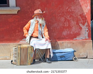 Warsaw - Poland. 27 July 2019: 
gray-haired old man sitting near accordion. Accordion stands next to old man with cigarette. Old musician earning his living by playing concertina. Old man street music