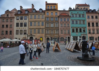 WARSAW / POLAND - AUGUST 15 2012: Well-dressed people stroll through artwork on display on A-frames in the Old Town Market Place, toward the old drinking fountain .