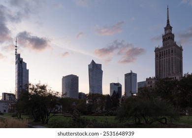 Warsaw skyline at dusk, featuring modern skyscrapers and the iconic Palace of Culture and Science, with a lush park in the foreground under a pastel-colored sky. High quality photo - Powered by Shutterstock