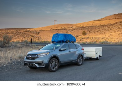 Wasco, Oregon / USA - October 1 2020: A blue Honda CR-V with a loaded roof rack wrapped in a tarp pullls a 1990 Coleman Columbia pop-up camper in rural Eastern Oregon. 