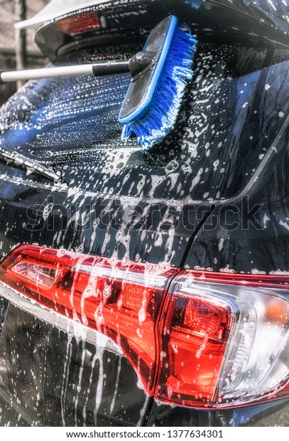 Wash a car on a sunny\
day. Use a brush and soap to wash a car in the driveway. hand in\
blurred motion. 