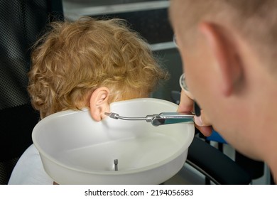 To Wash Ears With Water Irrigator, An Experienced Doctor Substitutes A Special Funnel To Child's Ear To Collect Water. Close-up Of Procedure For Cleaning Children's Ears From Ear Plugs In ENT Room