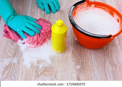 To Wash The Floor, Linoleum, Parquet. Hand In Rubber Gloves, A Bucket Of Soapy Water For Mopping And Damp Cleaning, Wet Pink Rag , Yellow Plastic Bottle With Detergent