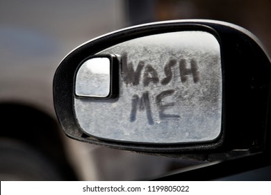 Wash Me Inscription On The Dirty Side View Mirror Of A Car