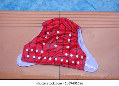 Washable red baby diaper swim trunk on thr floor beside the pool.