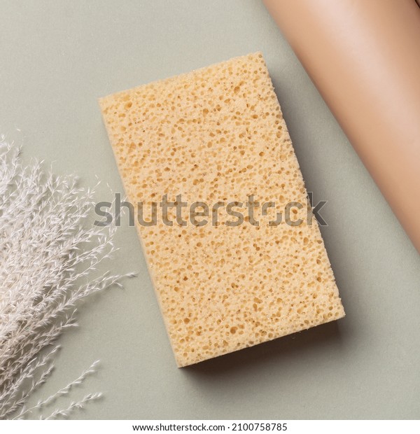 Washcloth sea\
sponge and dried flowers on green background. Foam sponge for\
shower or car. Yellow washcloth. Top\
view