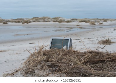 washed up crt tv / tube tv on a beach, partly covered with reed and surrounded by sand dunes - closeup with empty space