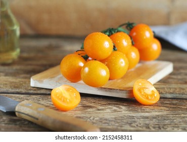 Washed orange cherry tomatoes lie on a board on a wooden table. Nearby are a towel, a knife. Behind is oil - Powered by Shutterstock